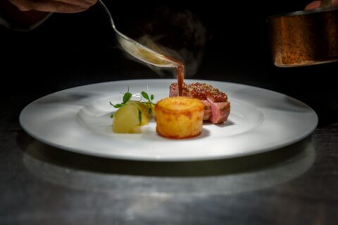 chef pouring sauce over plated steak