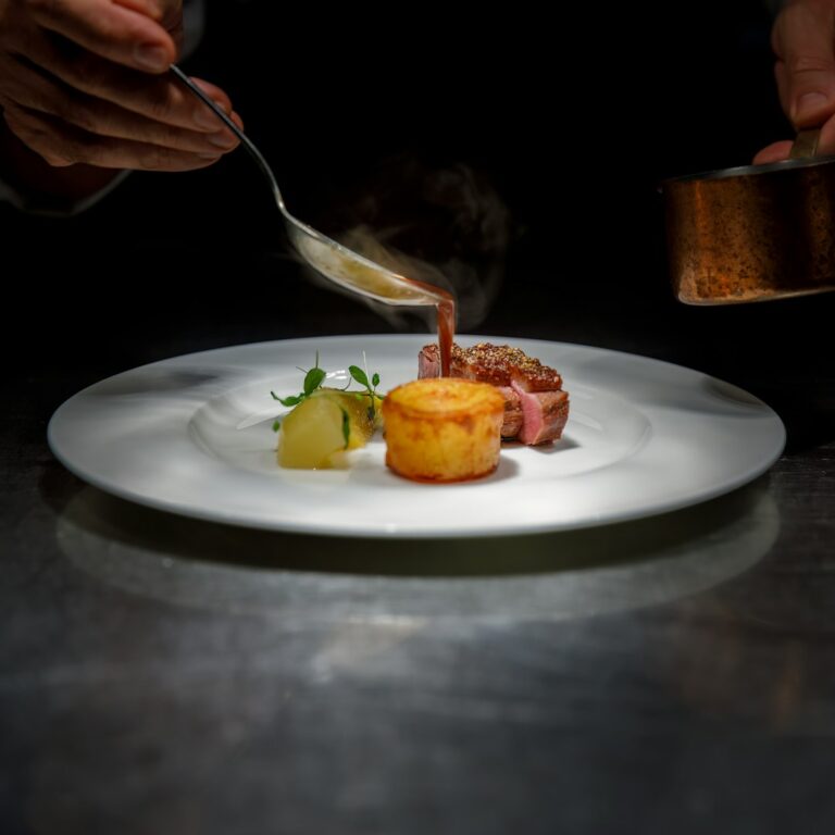 chef pouring sauce over plated steak