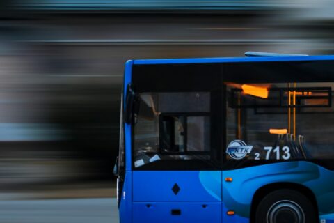 a blue bus driving down a street next to a tall building