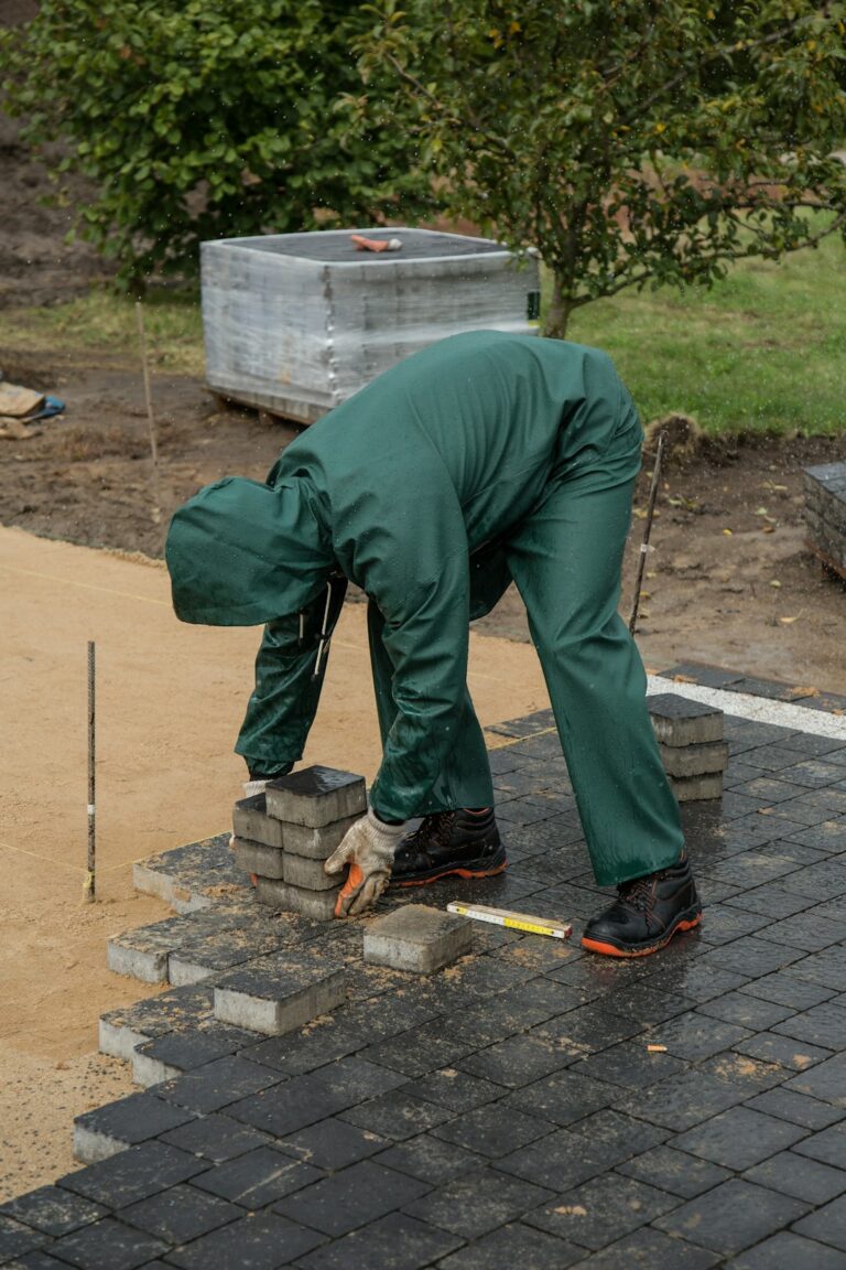a man in green pants and black shoes working on a brick wall