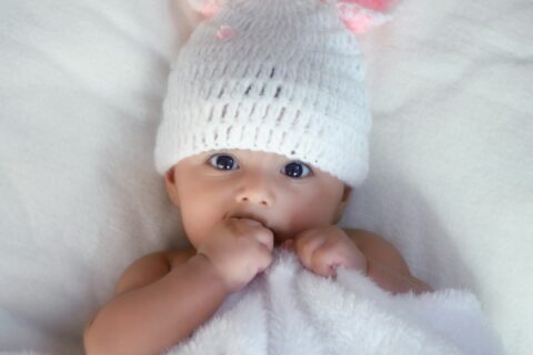 baby in white knit cap lying on white textile