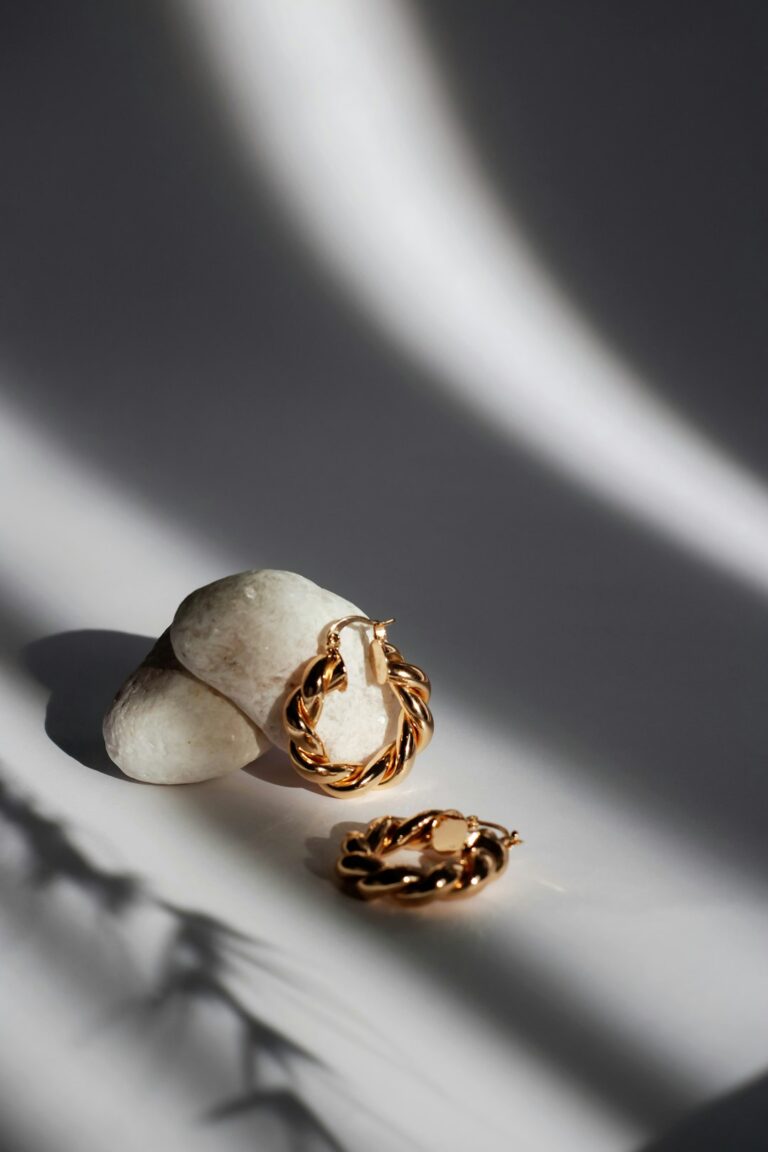 Two gold twisted hoop earrings resting on white stones with long shadows